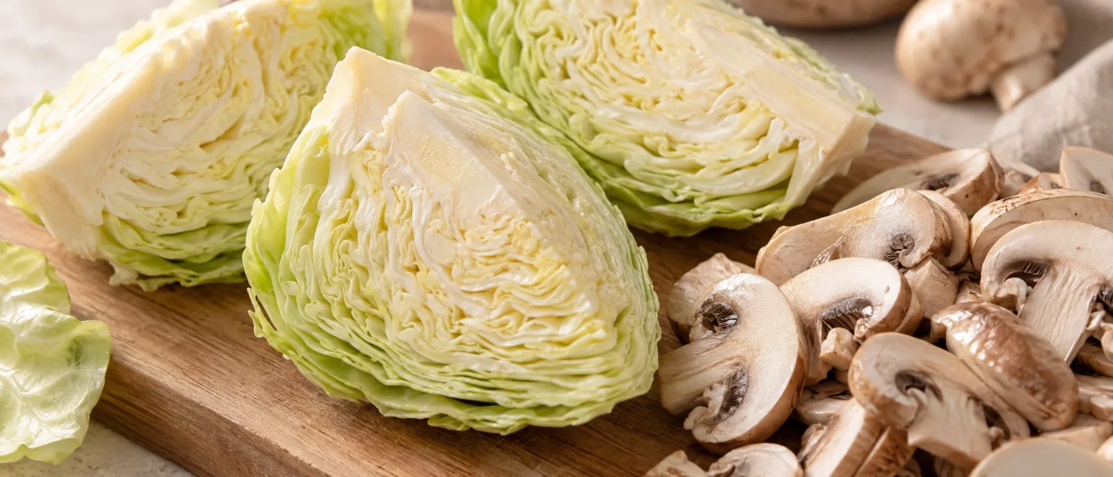 Raw white cabbage wedges retaining a section of core with sliced button mushrooms on a wooden board