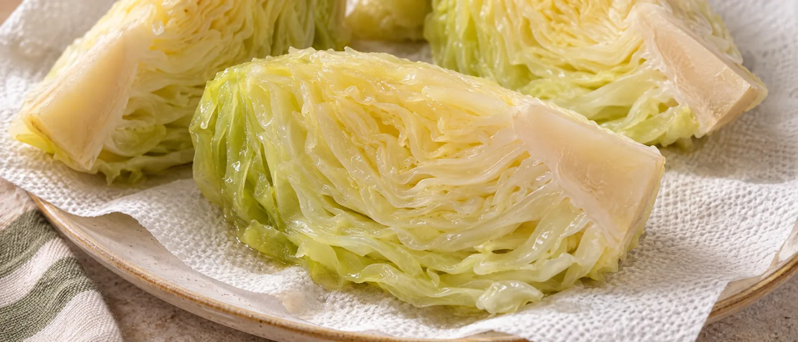 Cooked cabbage wedges retaining a section of core on kitchen paper laid over a plate